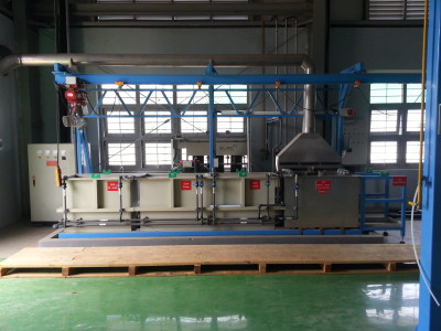 מכונה תעשייתית גדולה בתוך חלל מפעל מואר היטב. המכונה מצוידת ברכיבים מתכתיים שונים, צינורות ויחידות בקרה. ישנם שלטי אזהרה ותוויות באדום בחלקים מסוימים של הציוד. הרצפה ירוקה ומכוסה חלקית במשטח עץ.