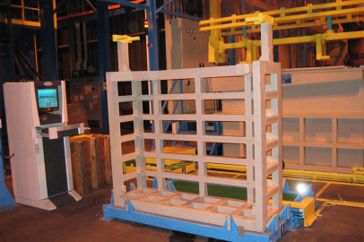 מסגרת מפעל עם מכונות. מרכזי הוא מבנה מתלה גדול ומתכת הנתמך בבסיס כחול, עם מחשב תעשייתי ולוח בקרה משמאל. ברקע נראים ציוד עילי צהוב ורכיבים תעשייתיים שונים.