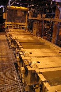 מתקן תעשייתי גדול עם סדרת מיכלים מלבניים מסודרים בשורה, כל אחד מחובר בצינורות ומכונות שונות. המבנה מכיל סורגי מתכת להליכה. מכונה צהובה ממוקמת בקצה אחד של שורת הטנקים. קיימת תאורה עמומה.