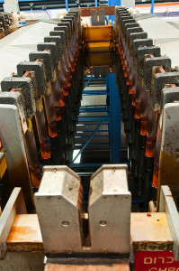 מבט מקרוב של מכונות תעשייתיות כבדות עם מספר רכיבי מתכת מקבילים ומוטות מיושרים אנכית. נראה שהציוד הוא חלק ממתקן ייצור או עיבוד, עם משטחים בלויים וחלק מהרכיבים מראים סימני חלודה.