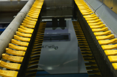 חפצי פלסטיק צהובים מיושרים בשורות מקבילות על מסוע תעשייתי. הפריטים הצהובים מעוצבים באופן אחיד ונראה שהם נמצאים בשלבים ראשוניים של תהליך הרכבה או ייצור. ברקע מוצגים חלקים מהמכונות.