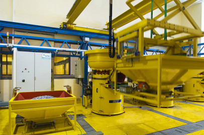 פנים מפעל עם מכונות וציוד תעשייתי צהוב. נראה פח צהוב גדול שמלא בחלקו בחומרים ומכונה נוספת בפעולה. המכונות כוללות מכולות, מבני מסועים ולוחות בקרה, והכל בפריסה מובנית.