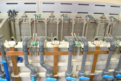 תמונה של מערך כור כימי במעבדה הכולל מכשירי זכוכית מרובים המחוברים לצינורות מתכת ושסתומים בעלי ידית כחולה. צינורות נחושת ופלסטיק מסודרים להעברת נוזלים, מה שמצביע על סביבת מעבדה מבוקרת לניסויים כימיים.